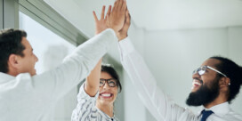 Three colleagues smiling and giving each other a high-five in a bright office setting.