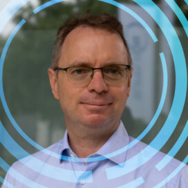Un homme portant des lunettes et une chemise bleu clair est représenté avec une expression neutre. Des éléments graphiques circulaires bleus sont superposés à l'image.