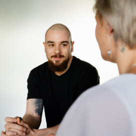 A man with a shaved head and beard sits across from a woman, engaging in conversation about career development for IT leaders in a bright indoor setting.