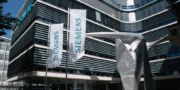 Two Siemens banners stand in front of a modern office building with a large metallic abstract sculpture in the foreground, highlighting the companys commitment to innovation and resourceful use of resources.