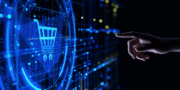 A hand points towards a glowing digital shopping trolley icon on a blue, futuristic touchscreen interface, representing online shopping technology.