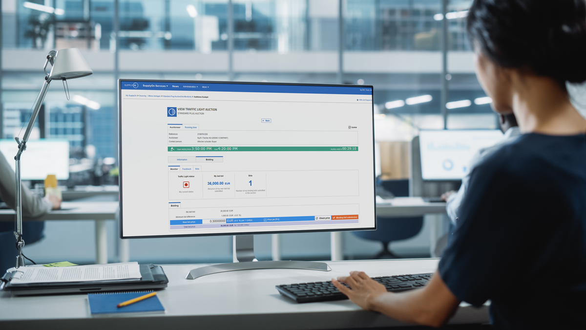A person sits at a desk in a modern office, viewing an online contract dashboard on a large computer monitor.