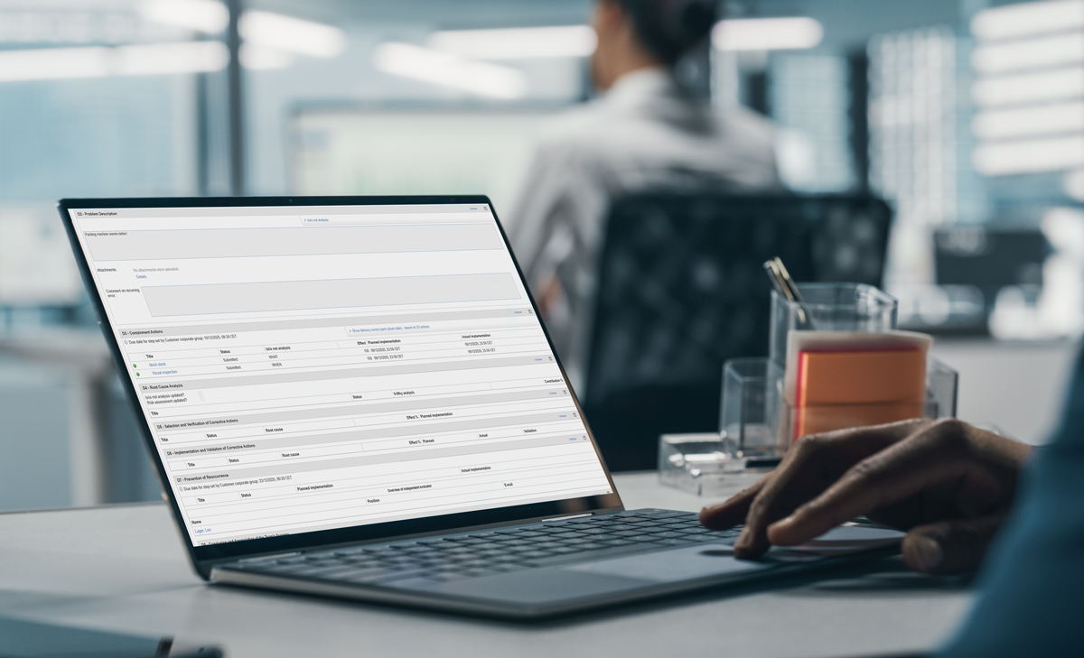 A person working on a laptop at an office desk, with a business management software interface open on the screen.