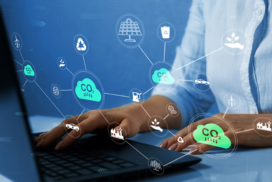Person typing on a laptop with illustrated icons representing carbon emissions, renewable energy, recycling, and environmental sustainability concepts overlaid on the image.