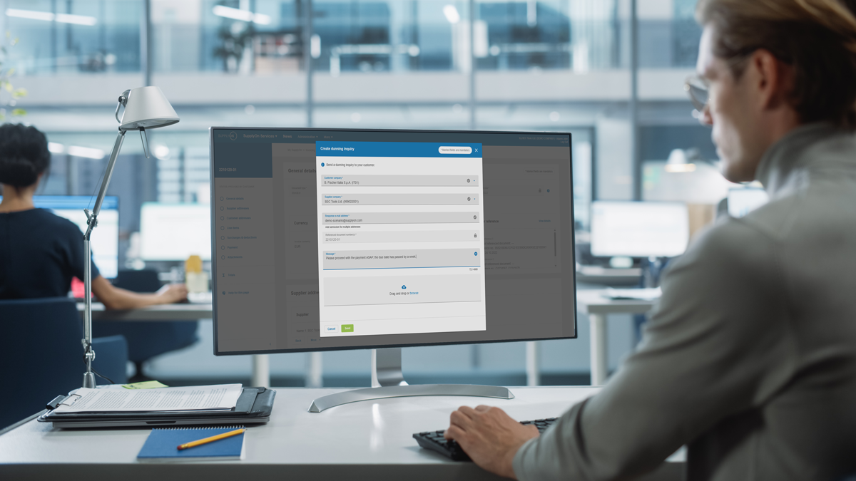 A person at a desk in an office uses a computer displaying an online form with fields and a progress bar.