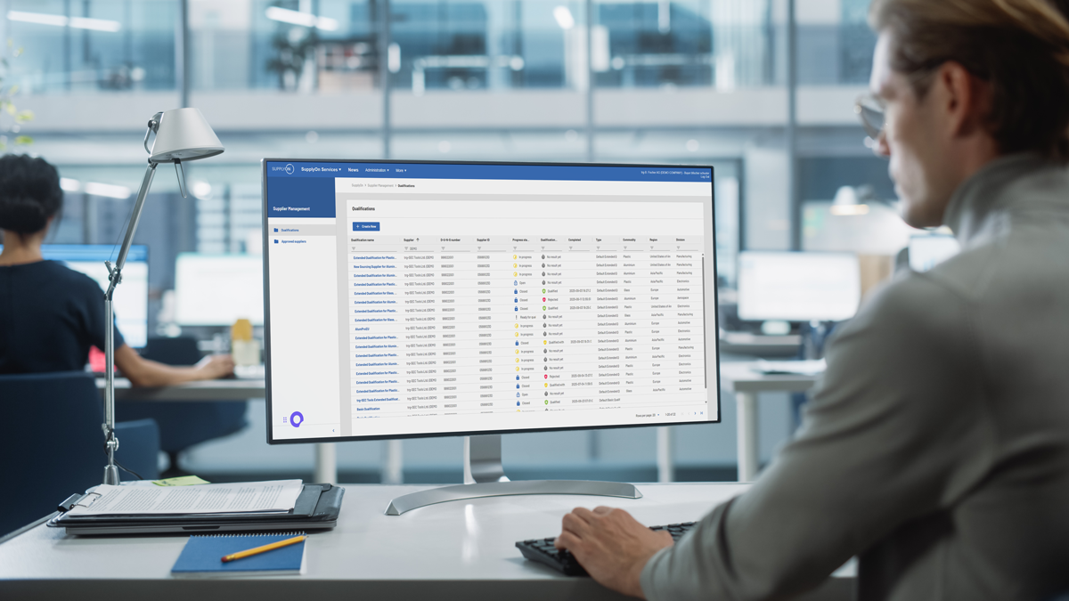 Person working at a desk, looking at a computer monitor displaying a data management dashboard with tables and coloured status indicators in a modern office setting.