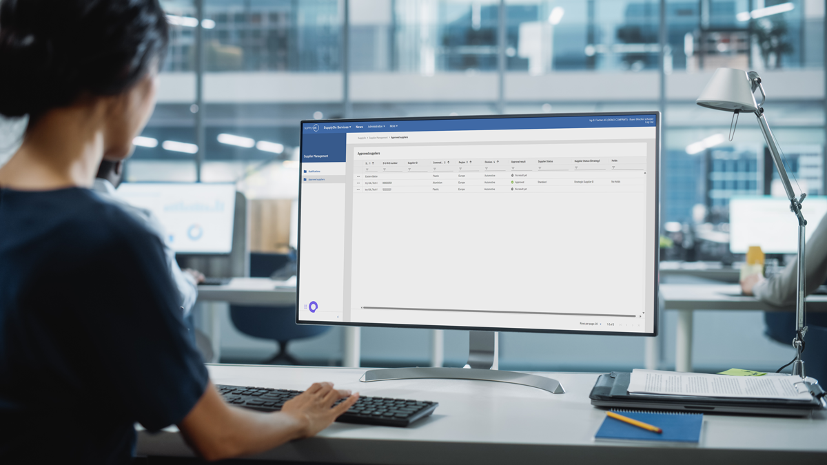 A person sits at a desk in an office, viewing a computer monitor displaying a data management or administration software interface.