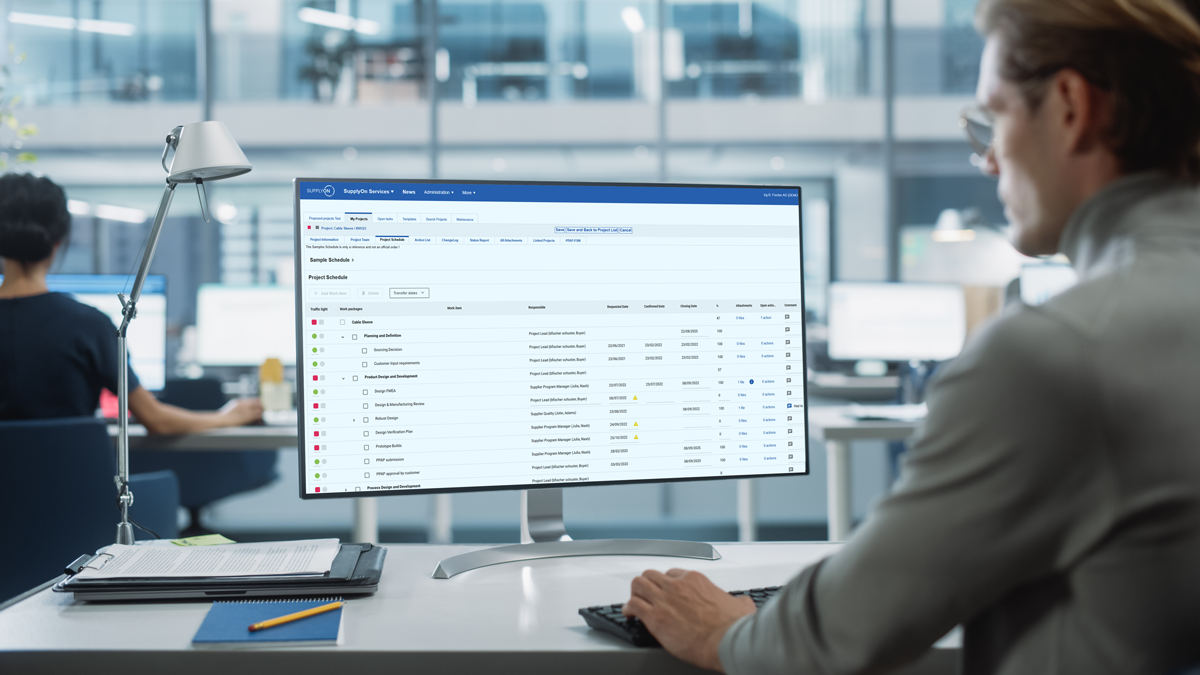 A person sits at a desk in an office, viewing a computer monitor displaying a data dashboard with tables and figures.