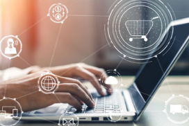 Hands typing on a laptop keyboard with overlay graphics of shopping trolley, cloud, money, and network icons representing digital business and e-commerce concepts.