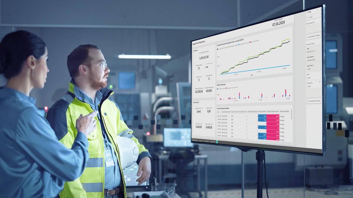 Two people in a modern industrial setting analyse data and charts displayed on a large monitor.
