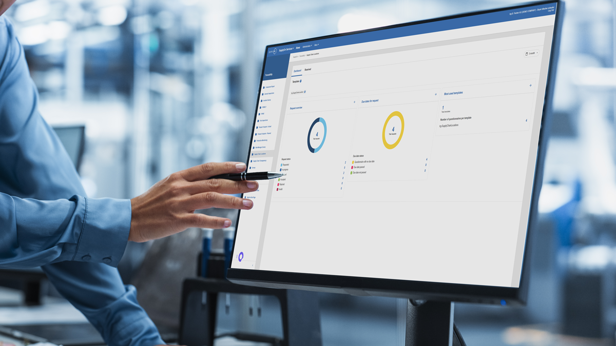 Person pointing at a computer monitor displaying analytics dashboards with circular charts and data on a management software interface in an office setting.
