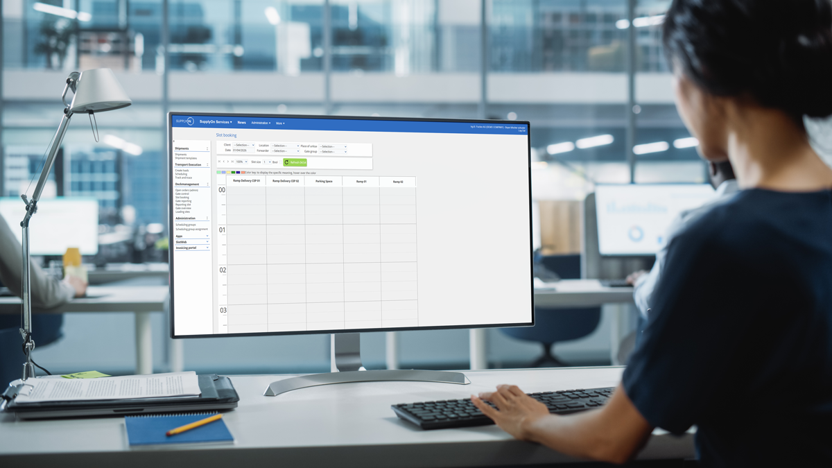 A person in an office uses a desktop computer displaying a scheduling or calendar application on the screen.