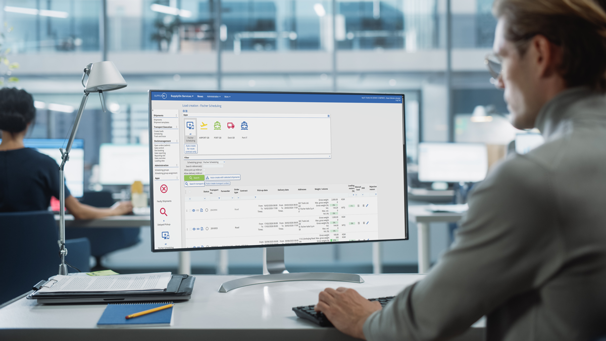 A person sits at a desk in an office, using a desktop computer displaying a software interface with lists, icons, and navigation menus.