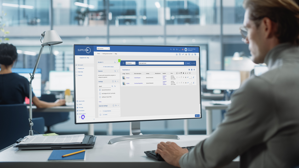 A person sits at a desk and works on a computer displaying supply management software in a modern office environment.