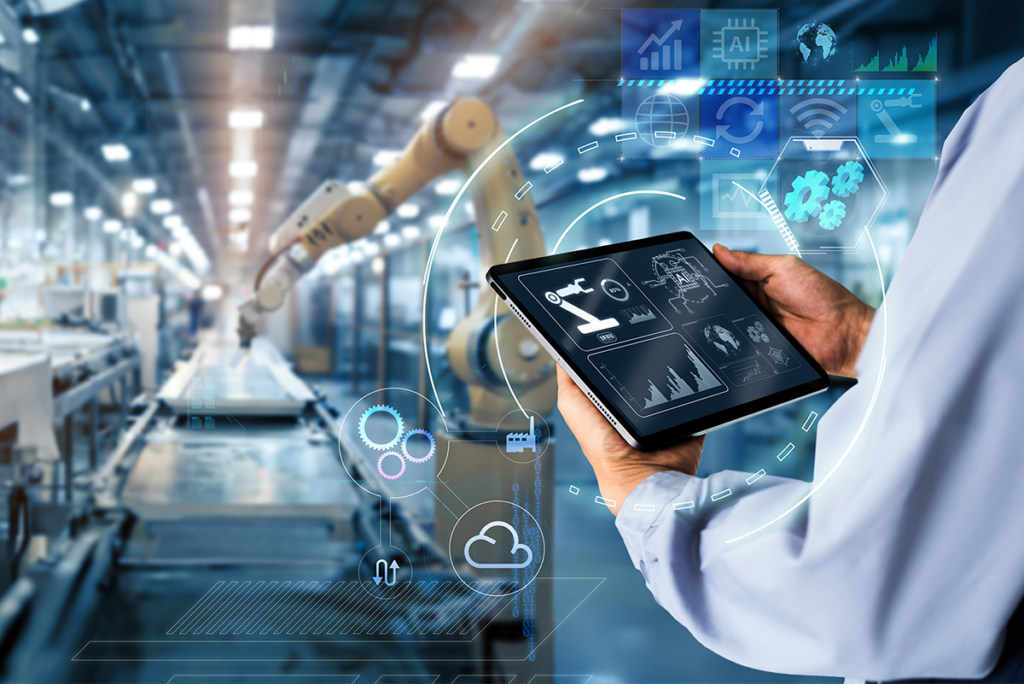 Person holding a tablet with digital graphs and icons in a modern factory, robotic arms and automated machinery visible in the background.